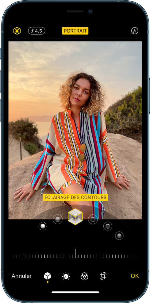 L’écran Modifier d’une photo prise en mode Portrait. En haut à gauche de l’écran se trouvent les boutons « Intensité de l’éclairage » et « Réglage de la profondeur ». En haut, au centre de l’écran, le bouton Portrait est activé. En haut à droite se trouve le bouton Annoter. La photo est au centre de l’écran ; sous celle-ci se trouve un curseur permettant de choisir l’effet d’éclairage de portrait. En dessous se trouve un curseur permettant d’ajuster la valeur de l’effet. En bas de l’écran, de gauche à droite, se trouvent les boutons Annuler, Portrait, Ajuster, Filtres, Recadrer et OK.