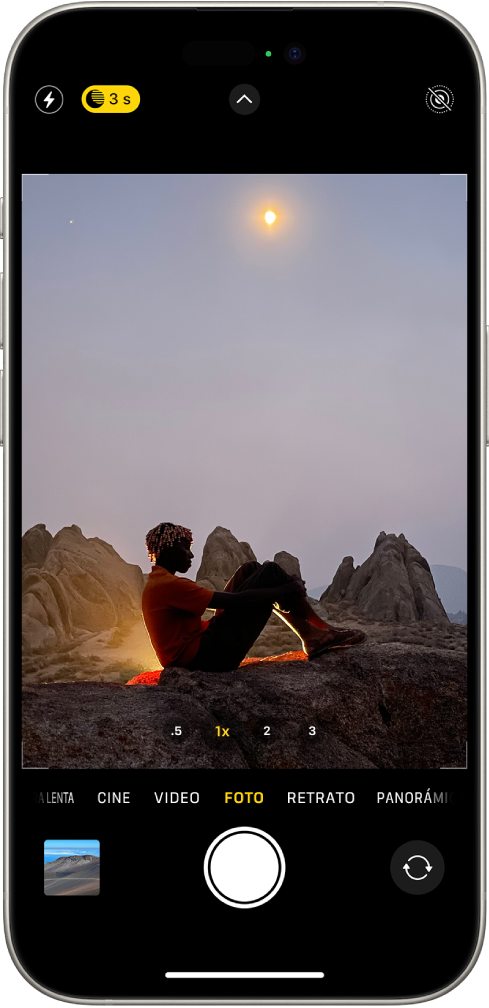 La pantalla de la app Cámara en el modo Foto. Los botones para el flash y el modo Noche aparecen en la esquina superior izquierda de la pantalla y el modo Noche está activado. El botón Controles de cámara está en la parte central superior, y el botón Live Photo está en la esquina superior derecha. En la parte inferior de la pantalla, de izquierda a derecha, se encuentran los botones Visor de fotos y videos, Tomar foto y Selector de cámara posterior. Dentro del encuadre de la cámara hay una escena nocturna.